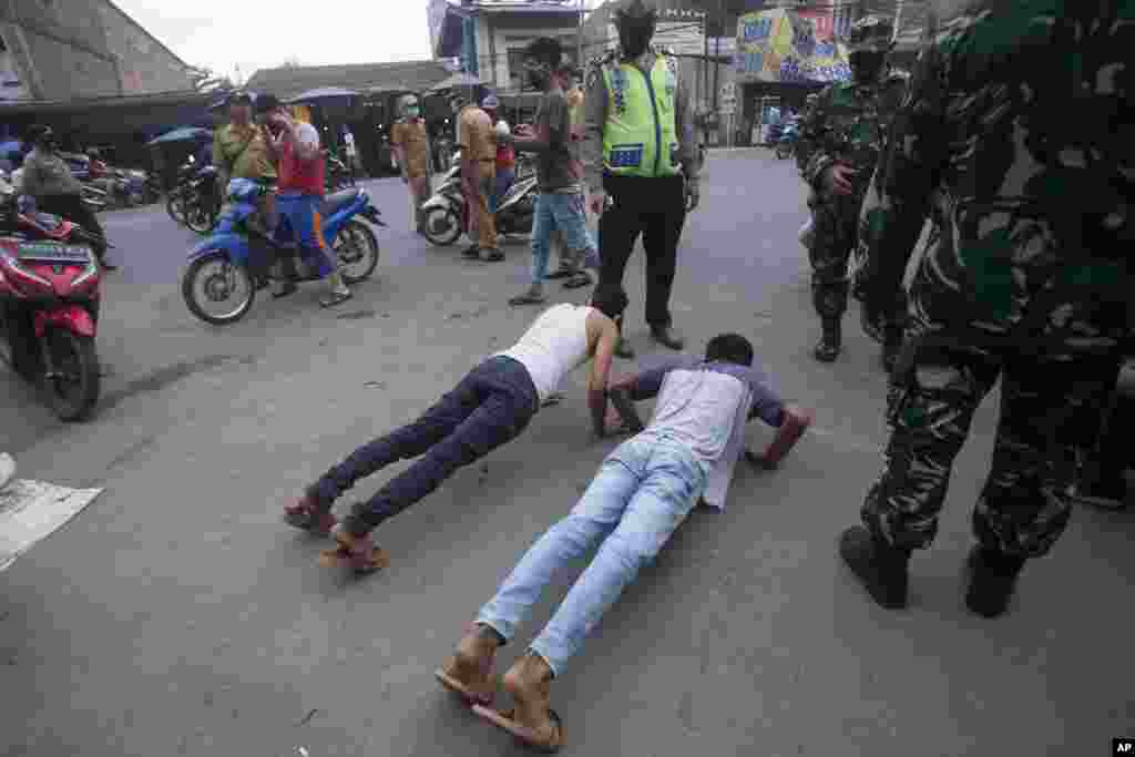 An Indonesian policeman and soldiers watch men do push-ups as a punishment for violating city regulation requiring people to wear face masks in public places as a precaution against coronavirus, in Medan, North Sumatra, Indonesia.