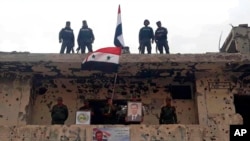 Des militaires syriens installent des drapeaux syriens sur un bâtiment endommagé dans le quartier de Hajar al-Aswad, au sud de Damas le 22 mai 2018.