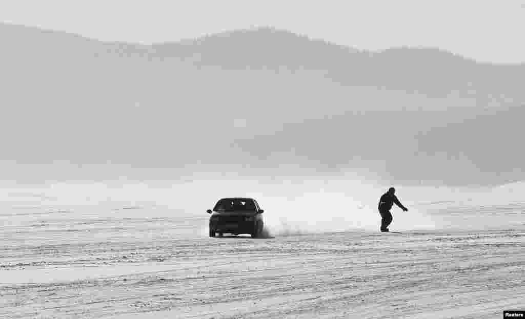 Sebuah mobil dengan seorang peselancar salju yang mengikuti di belakangnya melalui permukaan Sungai Yenisei yang beku di distrik Taiga, dengan suhu udara sekitar - 25&deg; C, di luar Krasnoyarsk, Siberia, Rusia.