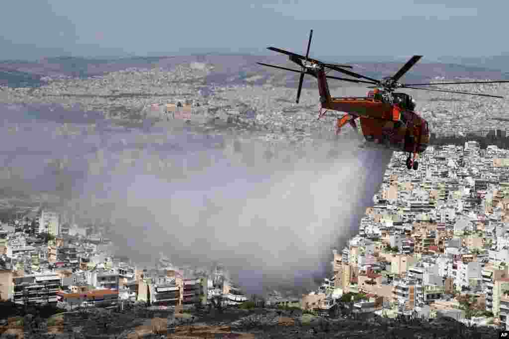 Sebuah helikopter menjatuhkan air di atas bukit yang dilanda kebakaran di pinggiran kota Vironas, sebelah timur Athena, sementara bukit Acropolis kuno tampak di latar belakang.