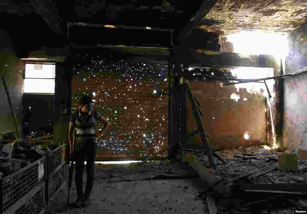 A Free Syrian Army fighter holds his weapon as he stands inside a burned shop in Aleppo's Karm al-Jabal district, Syria.
