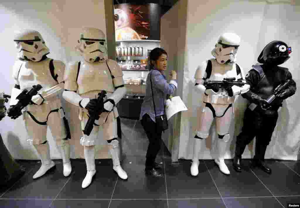 Seorang pegawai toko berjalan melewati pegawai lainnya yang berpakaian sebagai Stormtrooper dan Death Star Gunner (kanan) dari film &quot;Star Wars&quot; sebelum peluncuran mainan film tersebut di Loft Variety Store di pusat perbelanjaan Shibuya di Tokyo, Jepang.