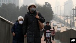 A woman and a child wearing masks walk hands in hands as a cyclist covers his nose for protection against the pollution on a pedestrian overhead bridge on a polluted day in Beijing, Sunday, Dec. 20, 2015.