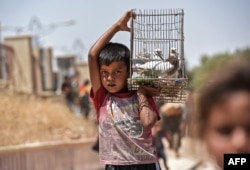 FILE - A displaced Iraqi boy carries a cage with pigeons as people arrive to a temporary camp at the compound of the closed Nineveh International Hotel in Mosul, June 16, 2017.