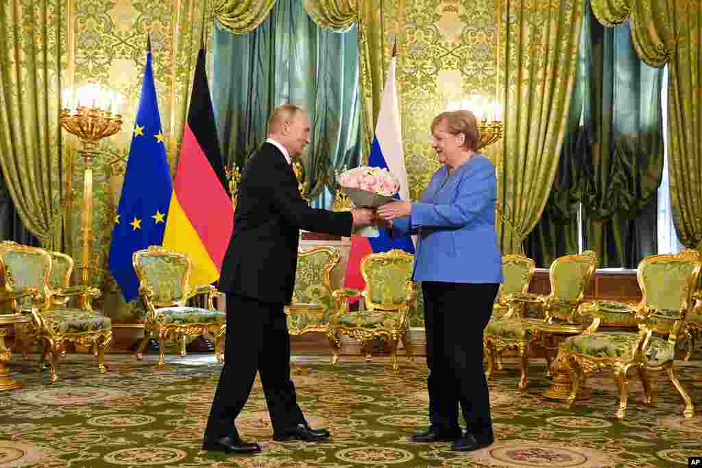 Russian President Vladimir Putin, left, presents flowers to German Chancellor Angela Merkel during their meeting in the Kremlin in Moscow, Russia. 