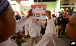 An electoral worker shows off a ballot paper with images of candidates during the gubernatorial election in Jakarta, Indonesia, Feb. 15, 2017.