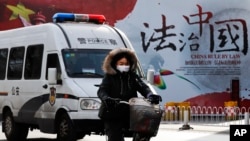A woman and a police van pass a Chinese government propaganda billboard that reads "China Rule By Law" on a street in Beijing, Dec. 28, 2016. Infuriated by a decision by Beijing prosecutors to drop charges in a high-profile police brutality case, university alumni circles across China mobilized online this week with petition drives, posing to China's government an unusual challenge with its white-collar makeup and swiftly expanding nationwide reach. 