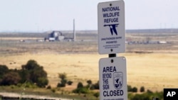 In this Wednesday, Aug. 14, 2019 photo, a sign designates a boundary of the Hanford Reach National Monument as the world's first large scale nuclear reactor, the B Reactor, is seen in the background where it sits unused on the Hanford Nuclear Reservation 