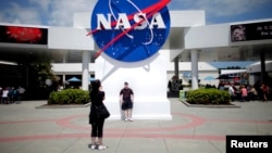 FILE - Tourists take pictures of a NASA sign at the Kennedy Space Center visitors complex in Cape Canaveral, Florida.