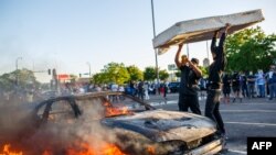 Des manifestants jettent un matelas sur une voiture en feu devant un magasin près du troisième commissariat de police le 28 mai 2020 à Minneapolis, dans le Minnesota, Etats-Unis. (Photo Kerem Yucel / AFP)