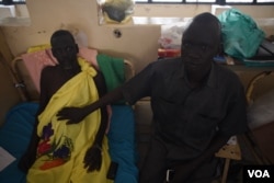 Michael Chieng Bol, right, holds his hand on his brother Simon's stomach, which is in need of further surgery following an operation to remove his appendix, in Juba Teaching Hospital, South Sudan's largest medical facility, May 23, 2016. (J. Patinkin/VOA)