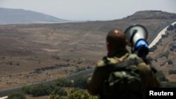An Israeli soldier speaks over a megaphone to people which stand next to the border fence between Israel and Syria from its Syrian side as it is seen from the Israeli-occupied Golan Heights near the Israeli Syrian border July 17, 2018. 