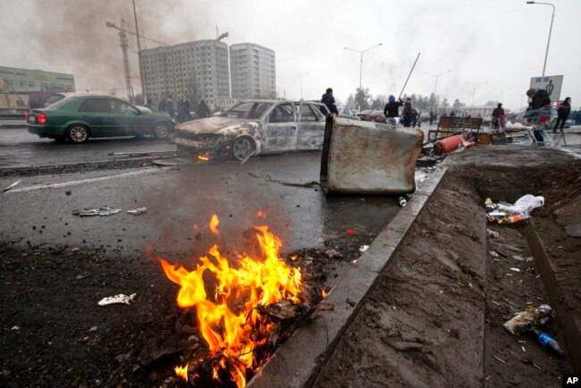 Warga berjalan melewati mobil-mobil yang terbakar setelah bentrokan, di sebuah jalan di Almaty, Kazakhstan, 7 Januari 2022. (Foto: AP)