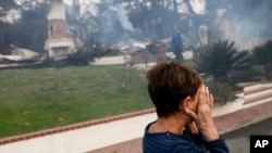 FILE - A woman cries as she covers her face near her destroyed home a wildfire swept through Ventura, California, Dec. 5, 2017. 
