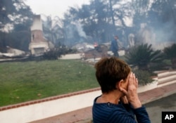 FILE - A woman cries as she covers her face near her destroyed home a wildfire swept through Ventura, California, Dec. 5, 2017.