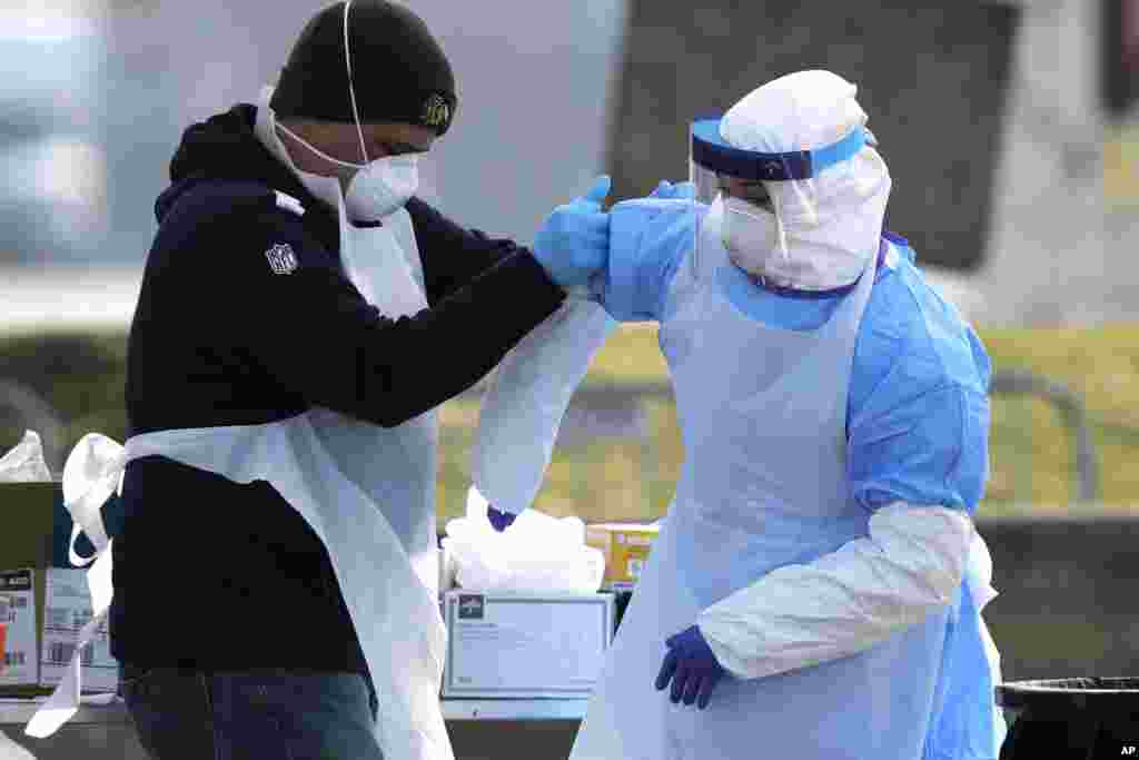 Medical personnel help each other at a federal COVID-19 drive-thru testing site in the parking lot of Walmart in North Lake, Illinois, March 25, 2020.