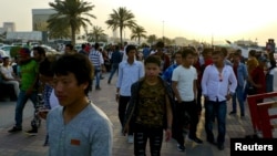 FILE - Migrant workers walk on the Corniche in Doha, Qatar. 