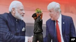 Un trabajador camina llevando flores para sembrar frente a una valla publicitaria con la foto del presidente de Estados Unidos, Donald Trump, y el primer ministro indio, Narendra Modi, en Agra, India, el domingo 23 de febrero de 2020.