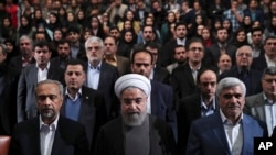In this photo released by official website of the office of the Iranian Presidency, President Hassan Rouhani, center, Science Minister Mohammad Farhadi, right, and head of the President's office Mohammad Nahavandian, left, listen to the national anthem at the start of a ceremony marking Student Day at Tehran University in Tehran, Iran, Tuesday, Dec. 6, 2016.