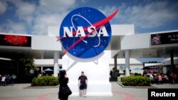 FILE - Tourists take pictures of a NASA sign at the Kennedy Space Center visitors complex in Cape Canaveral, Fla. 