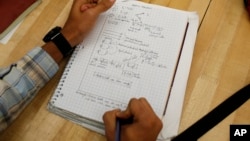 FILE - A student writes notes in the Advanced Placement Physics class at Woodrow Wilson High School in Washington, D.C., February 2014.
