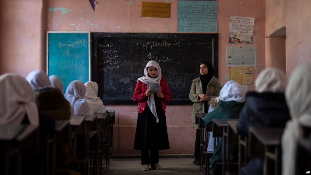 FILE - An Afghan girl reads in a classroom next to her teacher at Tajrobawai Girls High School, in Herat, Afghanistan, Nov. 25, 2021. Schools in Afghanistan are closed to girls beyond sixth grade.