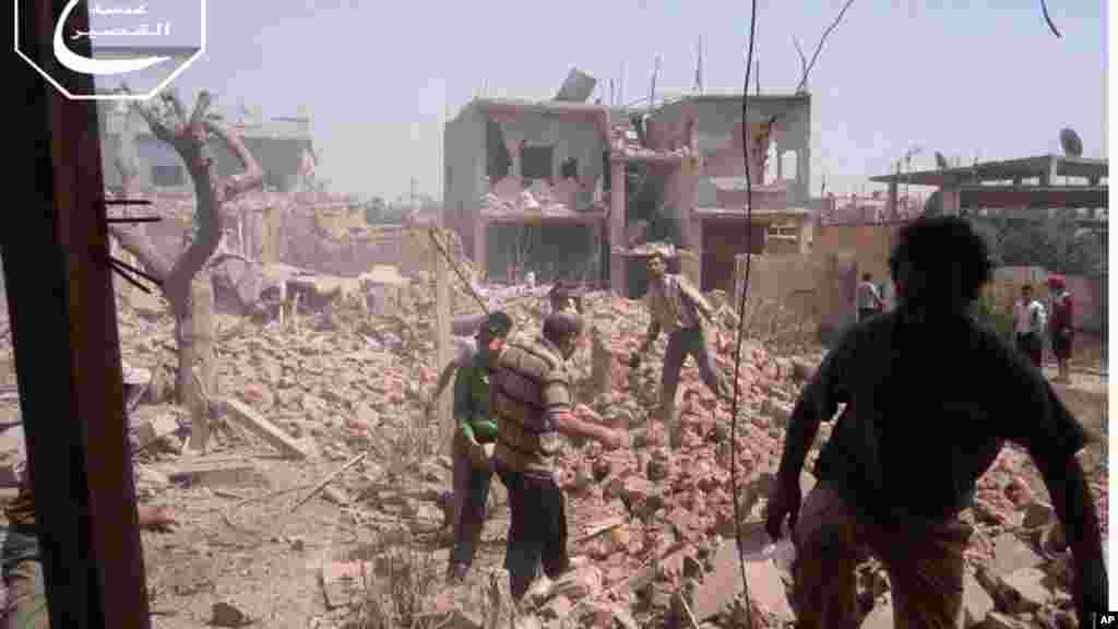 This citizen journalism image provided by Qusair Lens shows Syrians inspecting the rubble of buildings damaged in government airstrikes, in Qusair, Homs province, Syria, May 18, 2013.