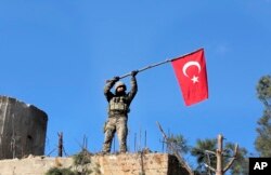 FILE - A soldier waves a Turkish flag as Turkish troops secure Bursayah Hill, which separates the Kurdish-held enclave of Afrin from the Turkey-controlled town of Azaz, Syria, Jan. 28, 2018.