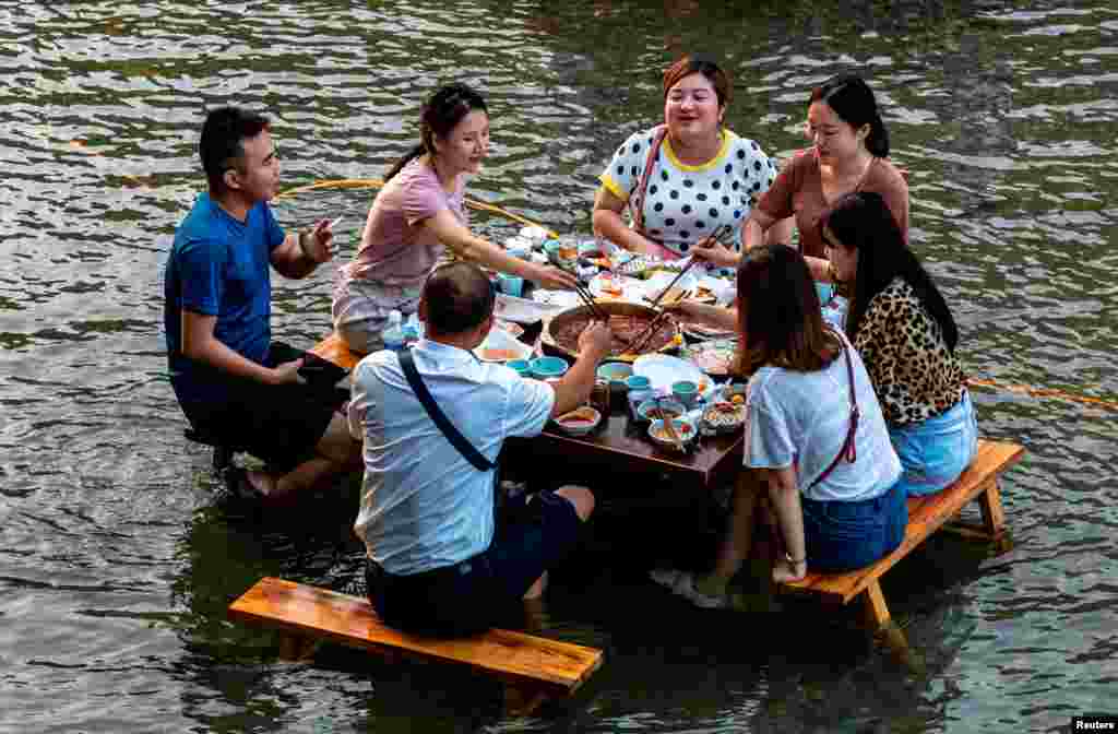 People eat hotpot at a table set up in a creek, inside a tourist attraction on a hot day in Chongqing, China, Aug. 21, 2018.