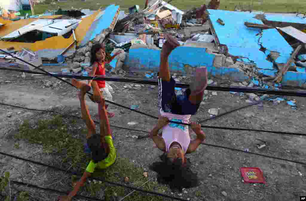Anak-anak bermain dengan kabel listrik yang sudah rusak di dekat gedung sekolah yang rusak di Guiuan, Filipina (14/11). (AP/Dita Alangkara)