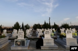 FILE - A woman sits among tombs in a cemetery during the funeral for a Syrian Democratic Forces fighter killed in the town of Hajin during battles against the Islamic State group, in the Kurdish-controlled city of Qamishly in northeastern Syria, Dec. 3, 2018.