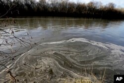 FILE - Signs of coal ash swirl in the water in the Dan River in Danville, Va., Feb. 5, 2014.
