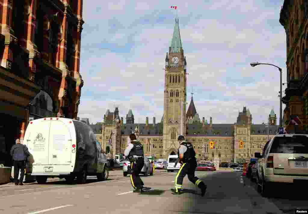 Armed RCMP officers race across a street on Parliament Hill following a shooting incident in Ottawa.