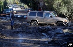 A man stands on a muddy road damaged from storms in Montecito, Calif.,, Jan. 11, 2018. Rescue workers slogged through knee-deep ooze and used long poles to probe for bodies as the search dragged on for victims of the mudslides that slammed this wealthy coastal community.
