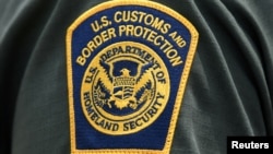 Në një uniformë shfaqet logoja e Agjensisë për Mbrojtjen e Kufirit dhe Doganave, pjesë e Departamentit të Sigurisë Kombëtare të Shteteve të Bashkuara