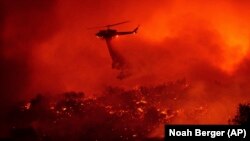 FILE - A helicopter drops water on the Cave Fire burning along Highway 154 in Los Padres National Forest, Calif., above Santa Barbara on Tuesday, Nov. 26, 2019. (AP Photo/Noah Berger)