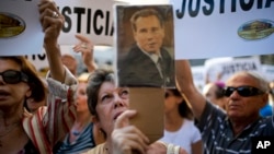 A woman sings the Argentine national anthem while holding a portrait of the late prosecutor Alberto Nisman outside the AMIA Jewish community center in Buenos Aires, Argentina, Jan. 21, 2015.