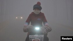 FILE - With a yellow smog alert in effect, a woman rides her electric bicycle along a street amid thick haze in Chiping county, Shandong province, China, Jan. 16, 2015.
