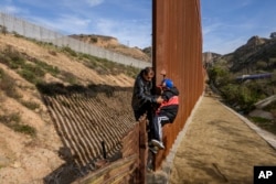 FILE - A Honduran migrant helps his son to climb the U.S. border fence before jumping into the United States to San Diego, Calif., from Tijuana, Mexico, Dec. 22, 2018.