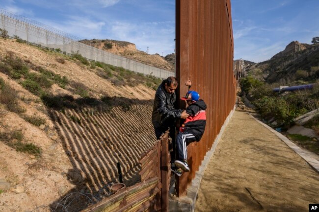 FILE - A Honduran migrant helps his son to climb the U.S. border fence before jumping into the United States to San Diego, Calif., from Tijuana, Mexico, Dec. 22, 2018.