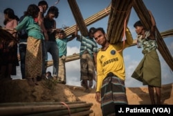 Rohingya refugees carry bamboo poles distributed by aid groups to reinforce shelters in the Kutupalong refugee camp. The aid groups are also handing out plastic sheeting.