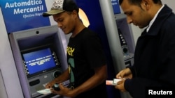 Men withdraw cash from automated teller machines at a Mercantil bank branch in Caracas, Venezuela, Aug. 20, 2018. 