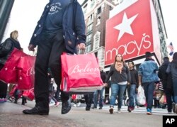 FILE - In this Friday, Nov. 27, 2015, file photo, shoppers carry bags as they cross a pedestrian walkway near Macy's in Herald Square, in New York.