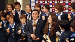 Japanese women's national soccer team coach Norio Sasaki, center, holding the World Cup trophy, poses with team players during a press conference in Tokyo, July 19, 2011.