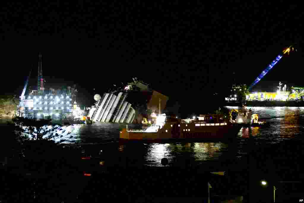 A ferry boat sails in front of the Costa Concordia ship lying on its side near the Tuscan Island of Giglio, Italy, Sept. 16, 2013.