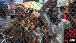 FILE - People stand behind a gate at Mpoko Airport in Bangui, Central African Republic, as food is being unloaded from a cargo aircraft.