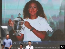 People walk by a huge screen showing US Open women's singles champion Naomi Osaka with her trophy, in Tokyo, Monday, Sept. 10, 2018. (AP Photo/Koji Sasahara)