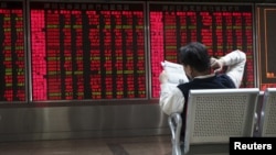 An investor reads a newspaper in front of electronic board showing stock information at a brokerage house in Beijing, China, Oct. 29, 2015. 