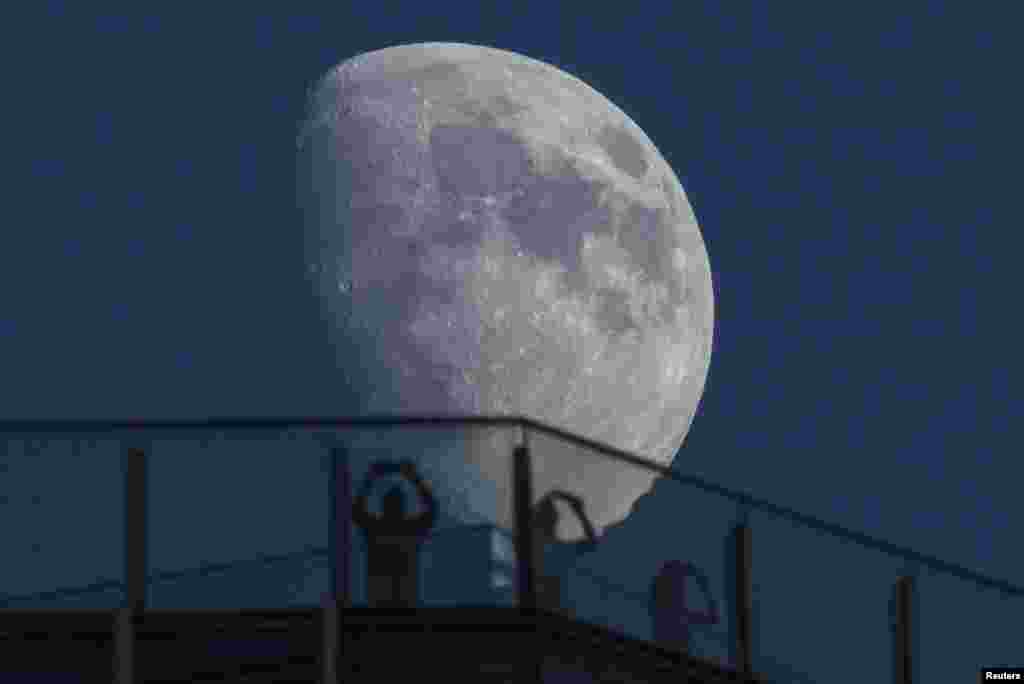 Visitors stand on the roof of a skyscraper as the moon rises over the skyline of Lujiazui financial district of Pudong in Shanghai, China.