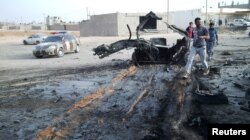 FILE - People inspect the site after a car bomb hit the convoy of Abdel-Razeq Nathouri, the chief of staff of the eastern Libyan military, outside Benghazi, Libya, April 18, 2018.
